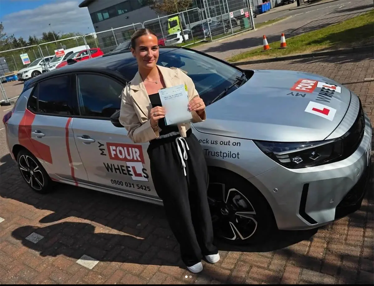A learner holding her practical driving test pass certificate beside a My Four Wheels car
