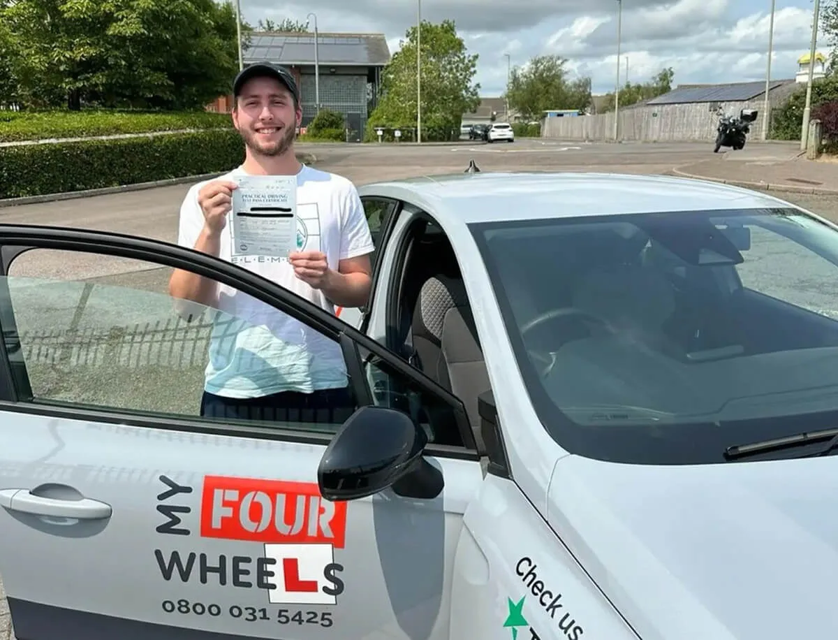 A learner holding his pass certificate beside a My Four Wheels lesson car