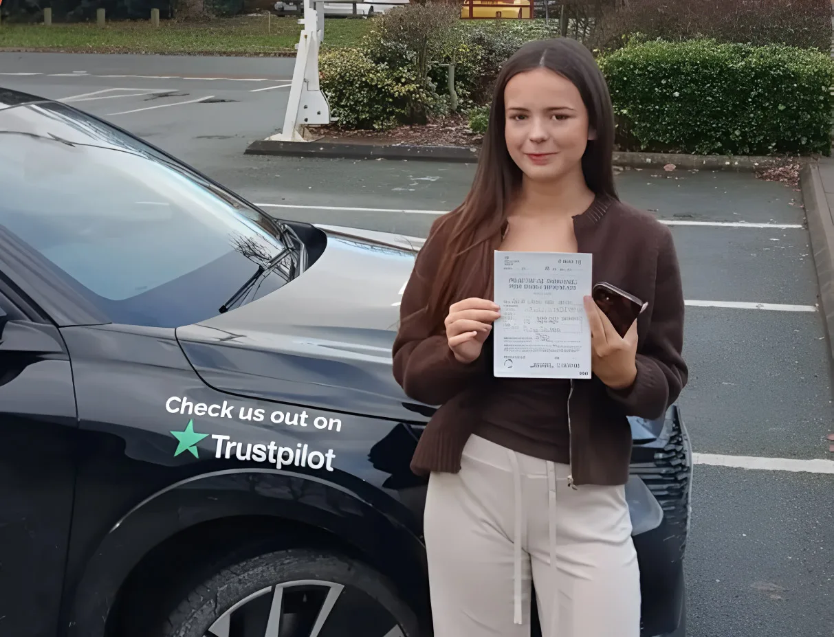 A learner holding her pass certificate beside a branded My Four Wheels car